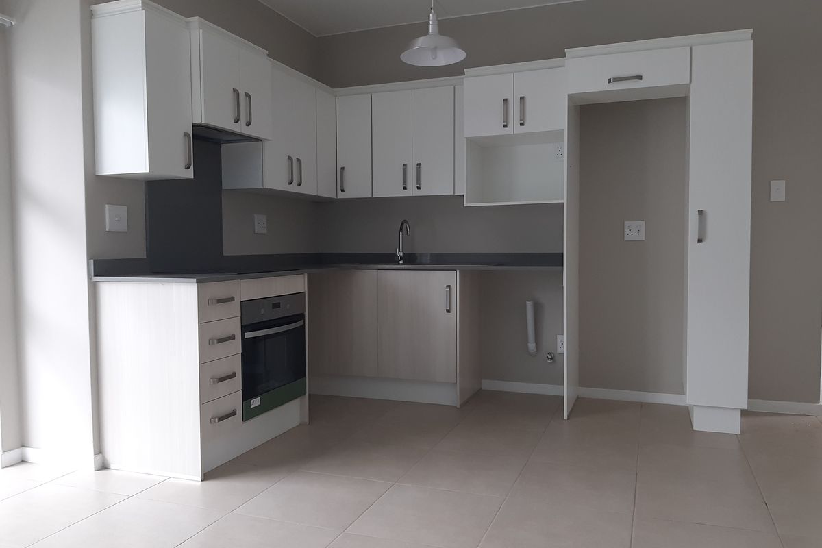 A clean, modern kitchen featuring white cabinetry, dark countertops, built-in oven, and tiled flooring. The space is vacant and ready for occupancy.