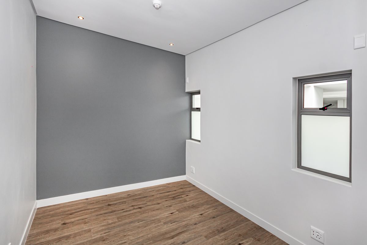 A clean, modern, and empty bedroom featuring neutral grey and white walls, laminate flooring, and recessed downlighting.