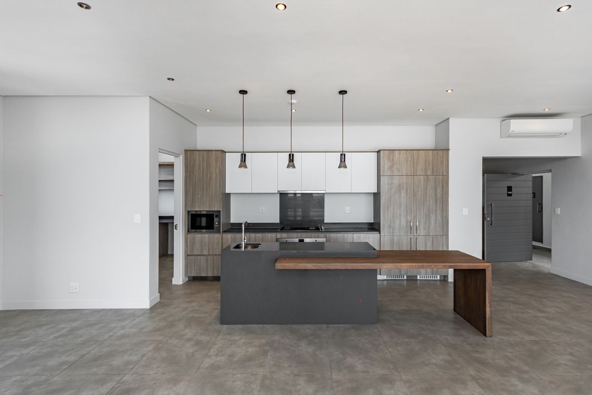 Modern kitchen featuring a central island with integrated sink and breakfast bar, sleek cabinetry, built-in appliances, and neutral tiled flooring.