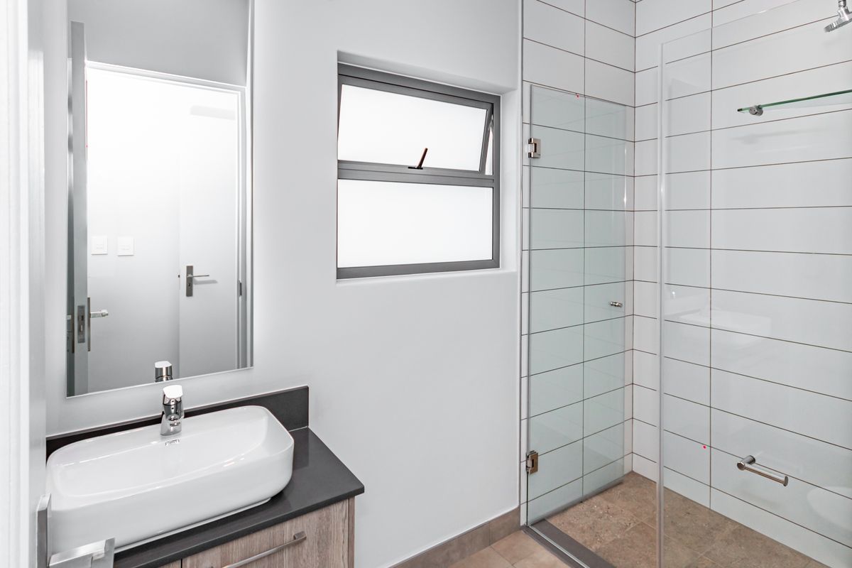 Modern bathroom featuring a vessel sink on a vanity cabinet, a large wall mirror, and a glass-enclosed shower with white tiled walls.