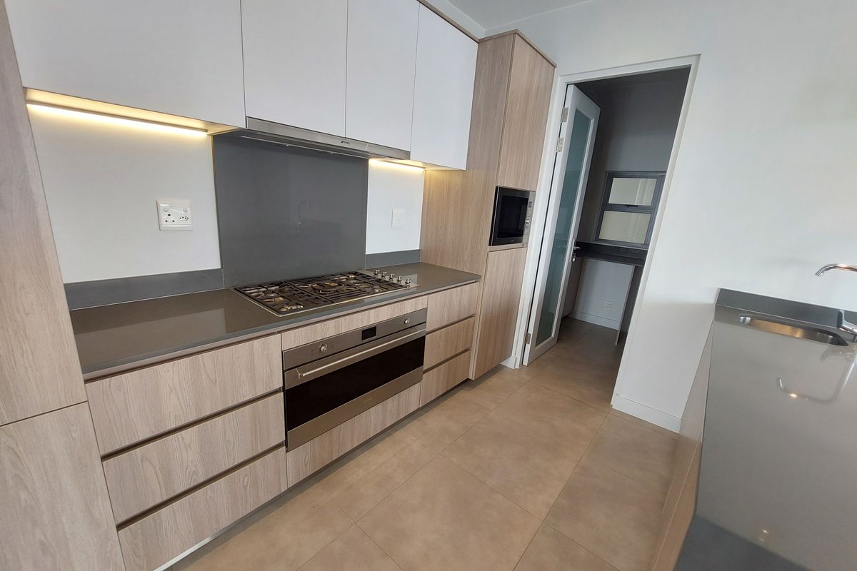 Modern kitchen featuring light wood-grain cabinetry, stone countertops, integrated gas hob, oven, and extractor fan, with sleek finishes and neutral tiled flooring.