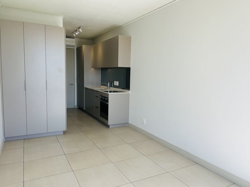 Modern open-plan apartment space featuring sleek built-in cabinetry, integrated kitchen appliances, neutral tiled flooring, and clean finishes throughout.