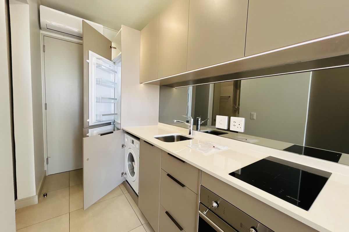 Modern, compact kitchen featuring integrated appliances, sleek cabinetry, mirrored splashback, induction hob, and built-in oven, finished with high-quality fixtures and tiled flooring.