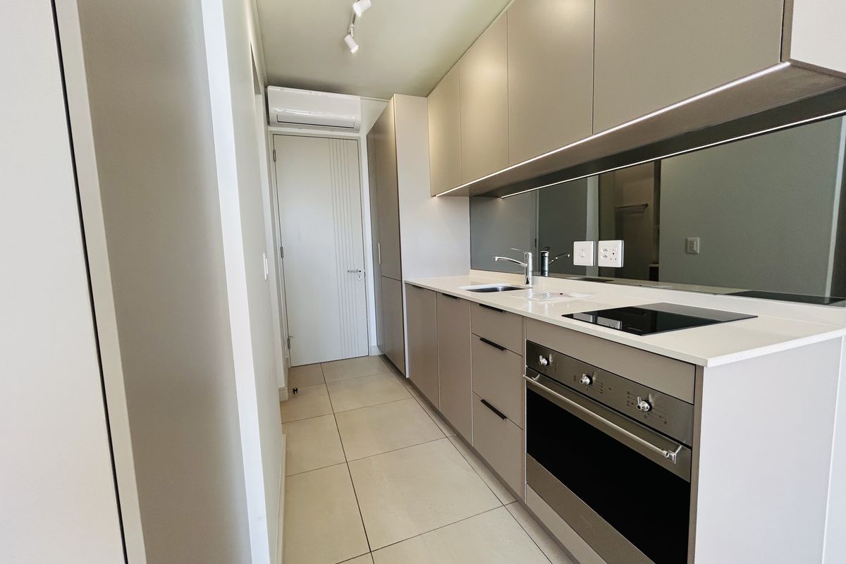 A modern, sleek kitchen featuring neutral cabinetry, stone countertops, integrated appliances, mirror splashback, and tiled flooring in a clean, contemporary layout.
