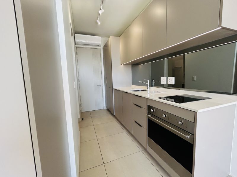 A modern, sleek kitchen featuring neutral cabinetry, stone countertops, integrated appliances, mirror splashback, and tiled flooring in a clean, contemporary layout.