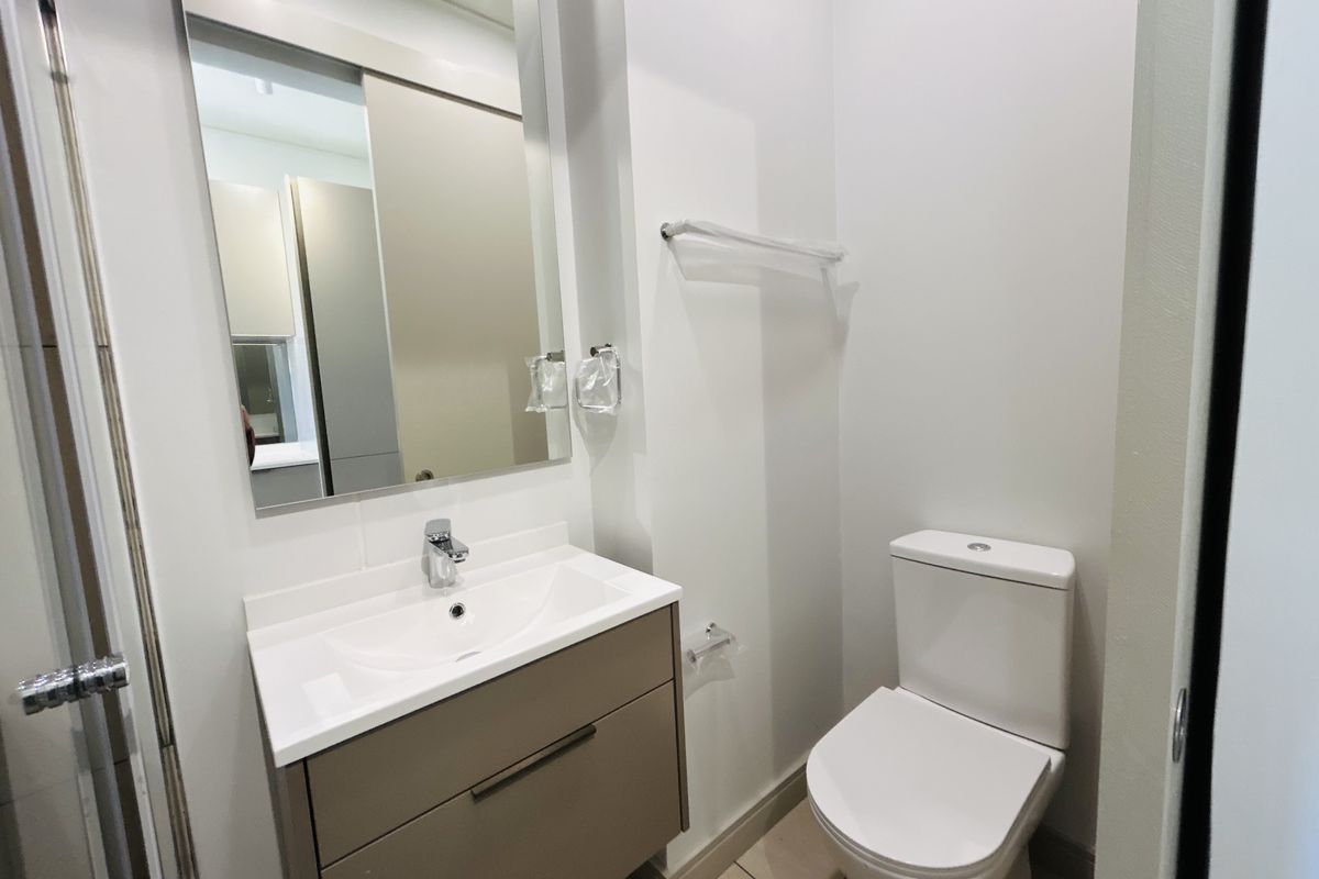 A clean and modern bathroom featuring a vanity cabinet with a basin, a wall-mounted mirror, and a standard toilet.