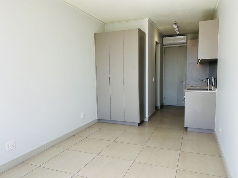 A modern open-plan living area featuring neutral tiled flooring, built-in storage cupboards, and a compact kitchen space with integrated fixtures.