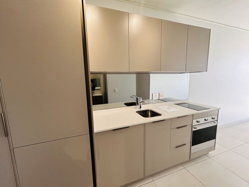 Modern compact kitchen featuring sleek handleless cabinetry, stone countertops, integrated oven and hob, and a mirrored splashback.