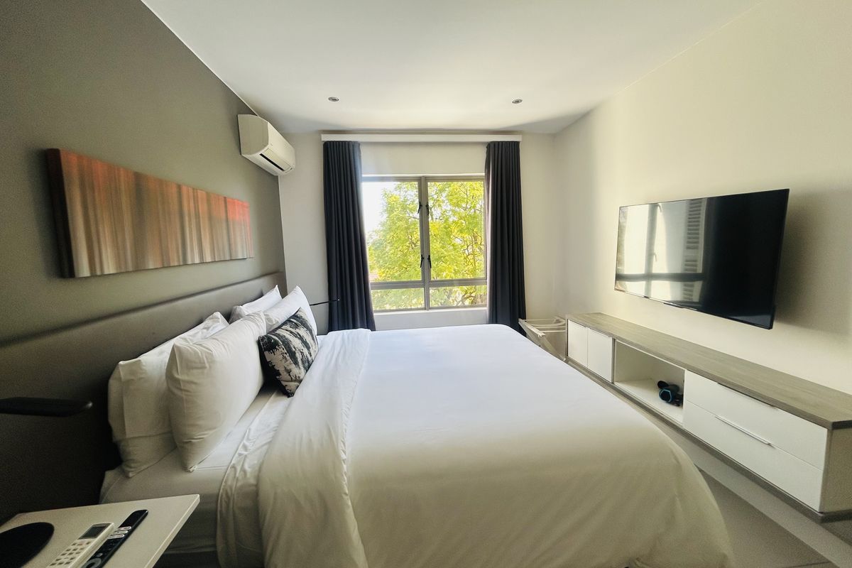 A well-maintained bedroom featuring a built-in media console, split-system air conditioning, and large windows providing natural light and a pleasant garden view.