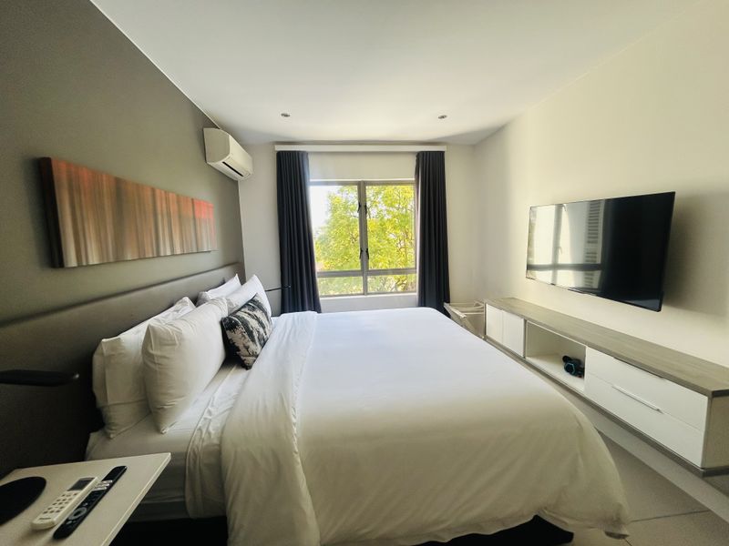 A well-maintained bedroom featuring a built-in media console, split-system air conditioning, and large windows providing natural light and a pleasant garden view.