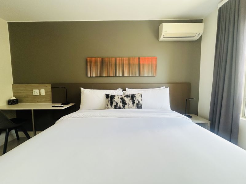 A well-maintained bedroom featuring a built-in headboard, integrated desk space, and a wall-mounted air conditioning unit.