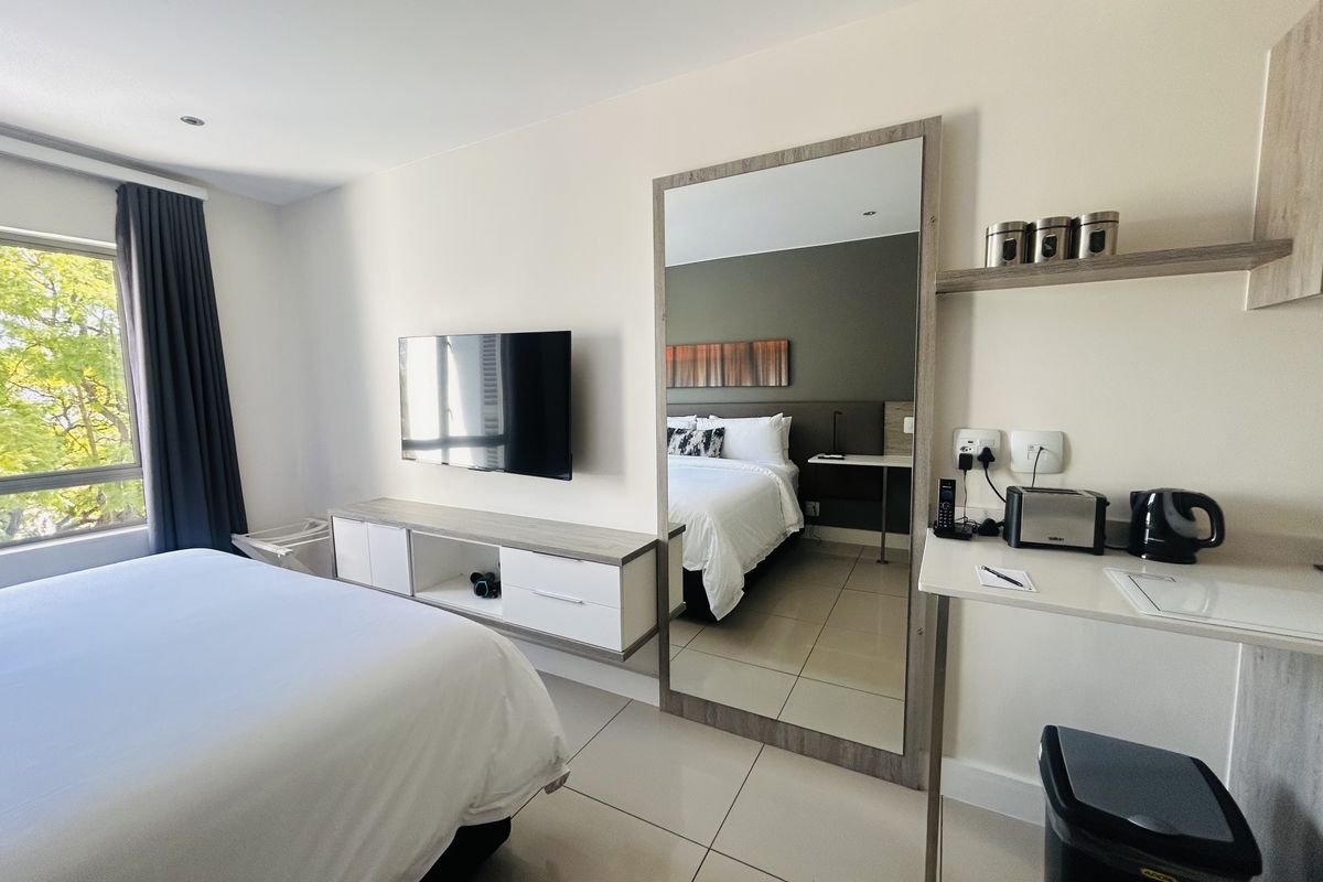 A modern bedroom featuring tiled floors, built-in cabinetry, a wall-mounted television, and a large full-length mirror, offering a clean and functional living space.