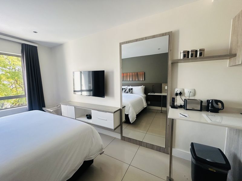 A modern bedroom featuring tiled floors, built-in cabinetry, a wall-mounted television, and a large full-length mirror, offering a clean and functional living space.