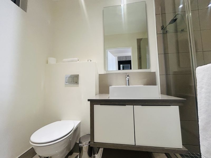Modern bathroom featuring a wall-hung toilet, contemporary vanity with vessel sink, wall mirror, and a glass-enclosed shower area with tiled finishes.
