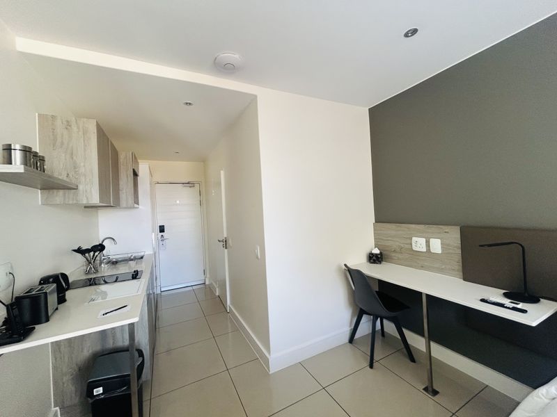 Modern open-plan apartment featuring a compact kitchenette with built-in cabinetry and a dedicated study area with a fitted desk.
