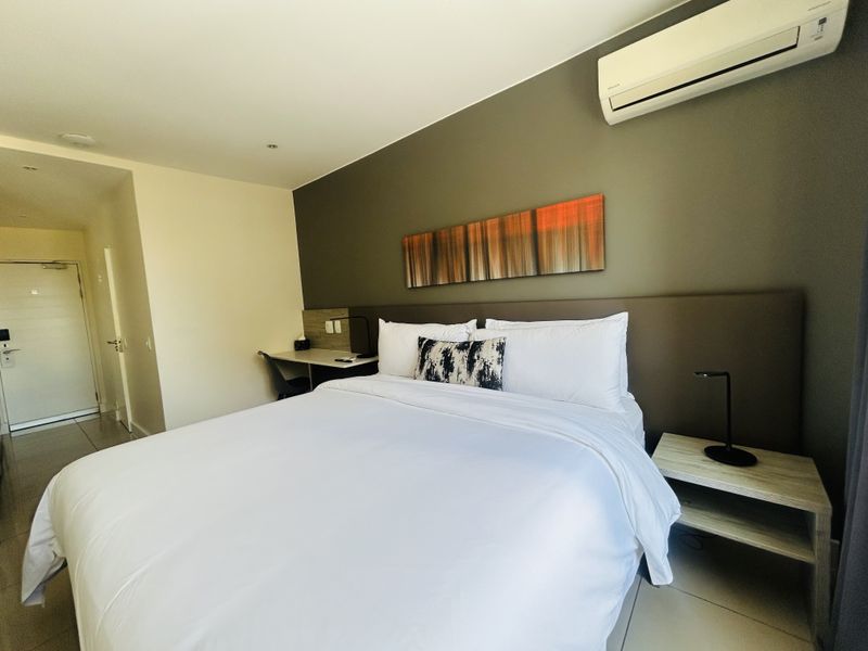 A modern bedroom featuring a built-in headboard, integrated desk space, tiled flooring, and a wall-mounted split-system air conditioner.