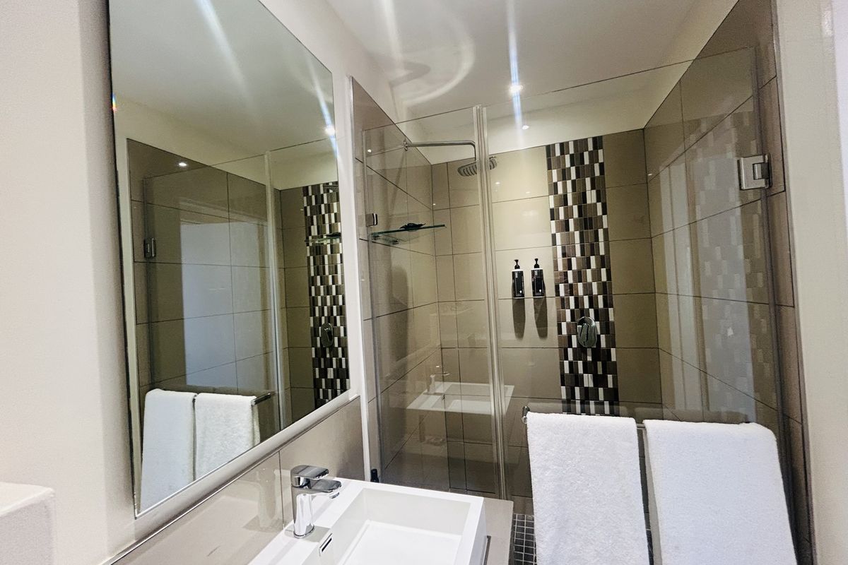 Modern bathroom featuring a glass-enclosed shower, contemporary basin with chrome mixer tap, and large wall-mounted mirror with neutral tiled finishes.