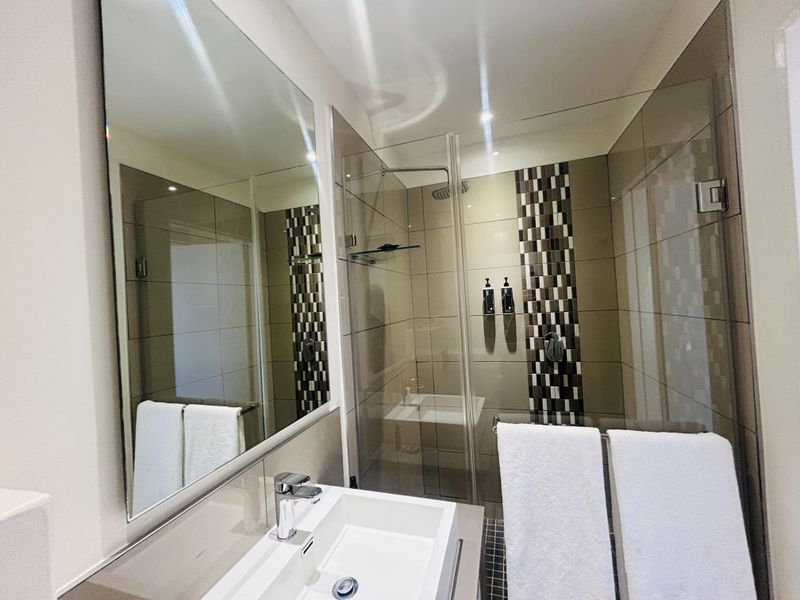 Modern bathroom featuring a glass-enclosed shower, contemporary basin with chrome mixer tap, and large wall-mounted mirror with neutral tiled finishes.