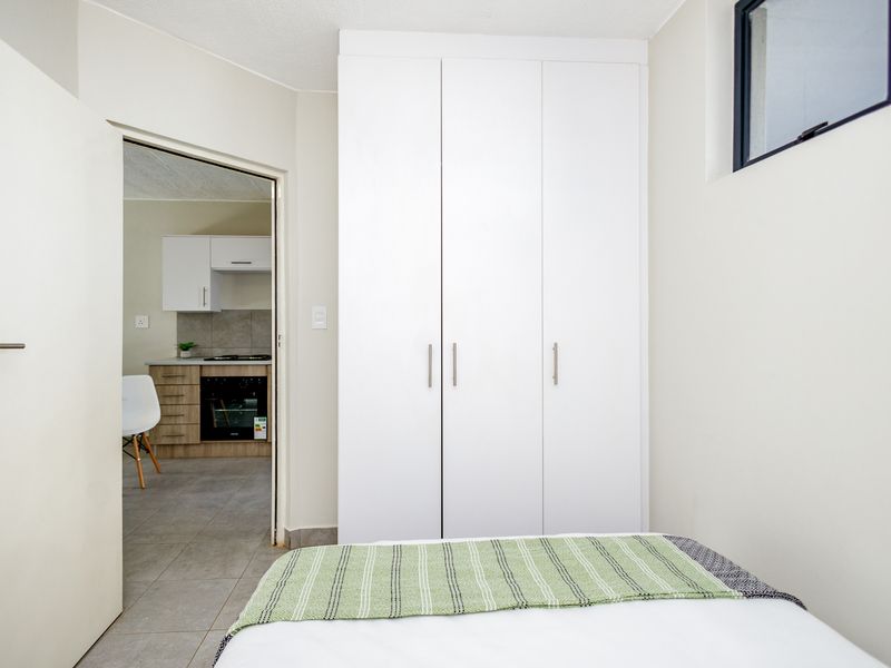 A clean bedroom featuring built-in white wardrobes, tiled flooring, and a view through to the adjacent kitchen area.