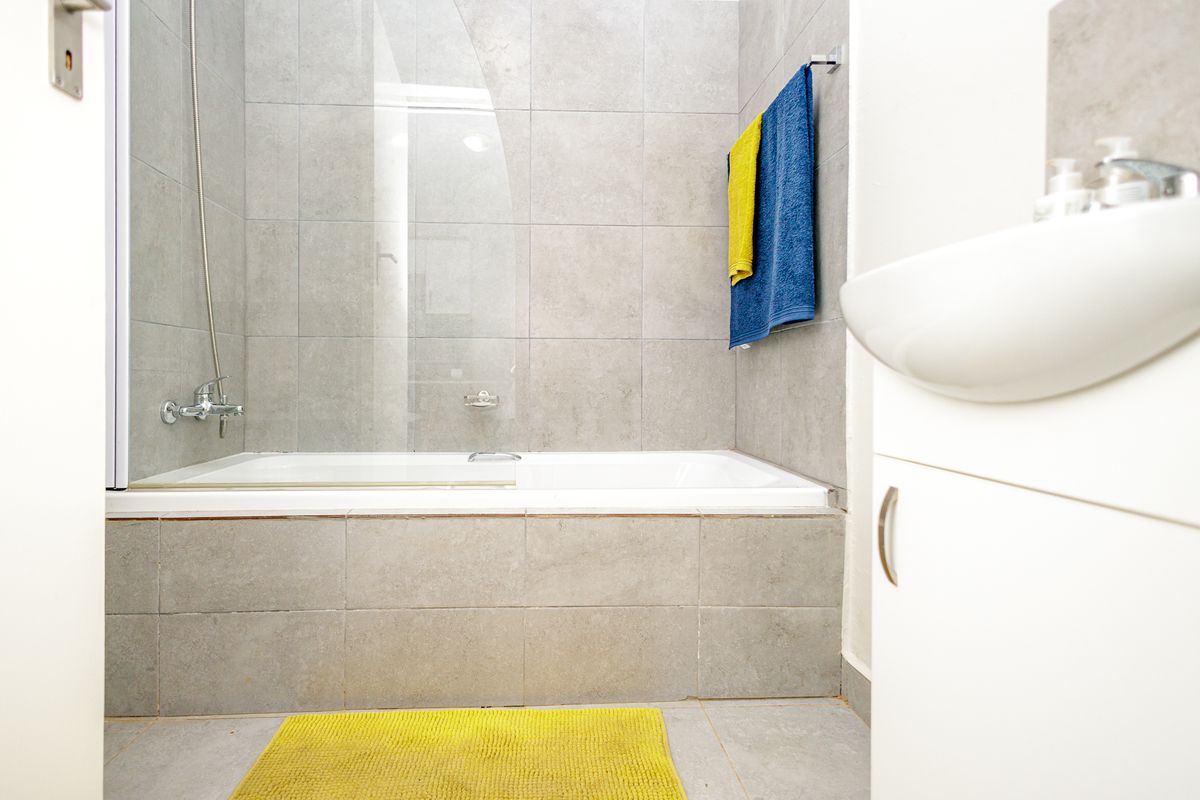 A modern bathroom featuring a bathtub with a glass shower screen, tiled walls, and a vanity basin.