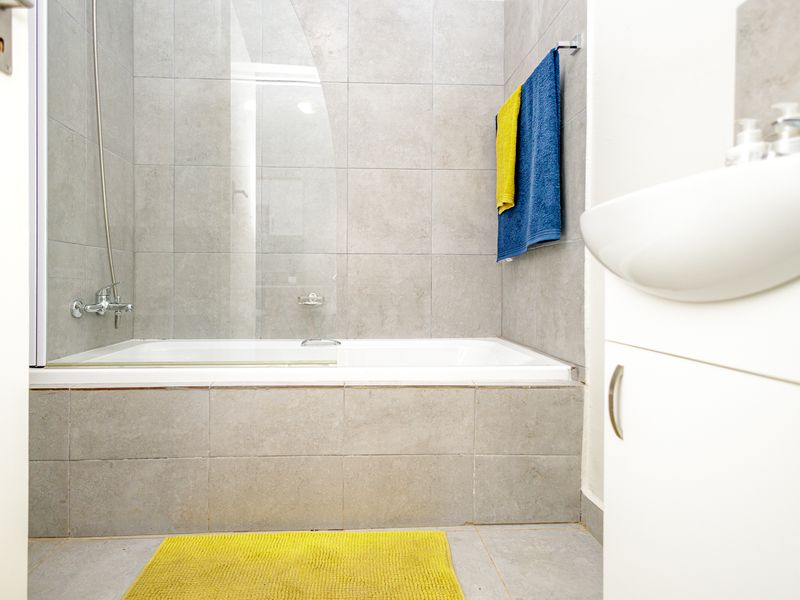 A modern bathroom featuring a bathtub with a glass shower screen, tiled walls, and a vanity basin.