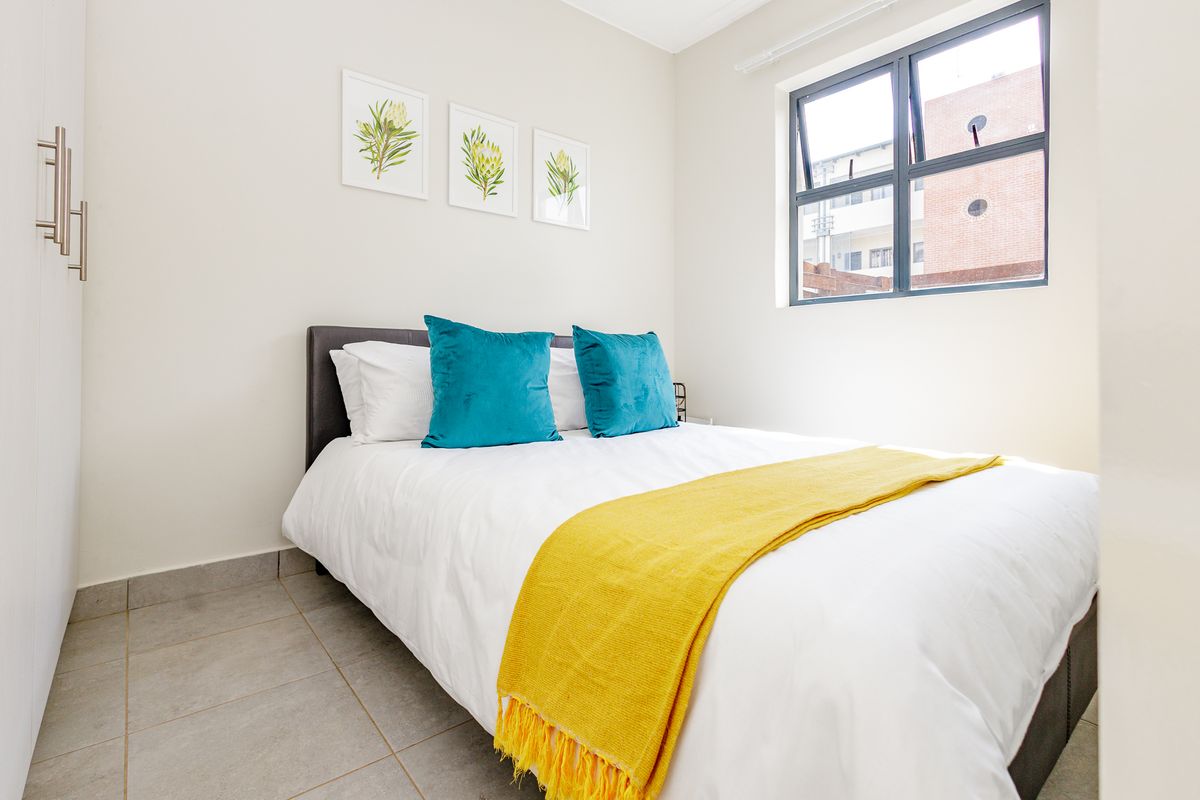A well-maintained bedroom featuring neutral tiled flooring, a built-in wardrobe, and a modern aluminium-framed window providing natural light.