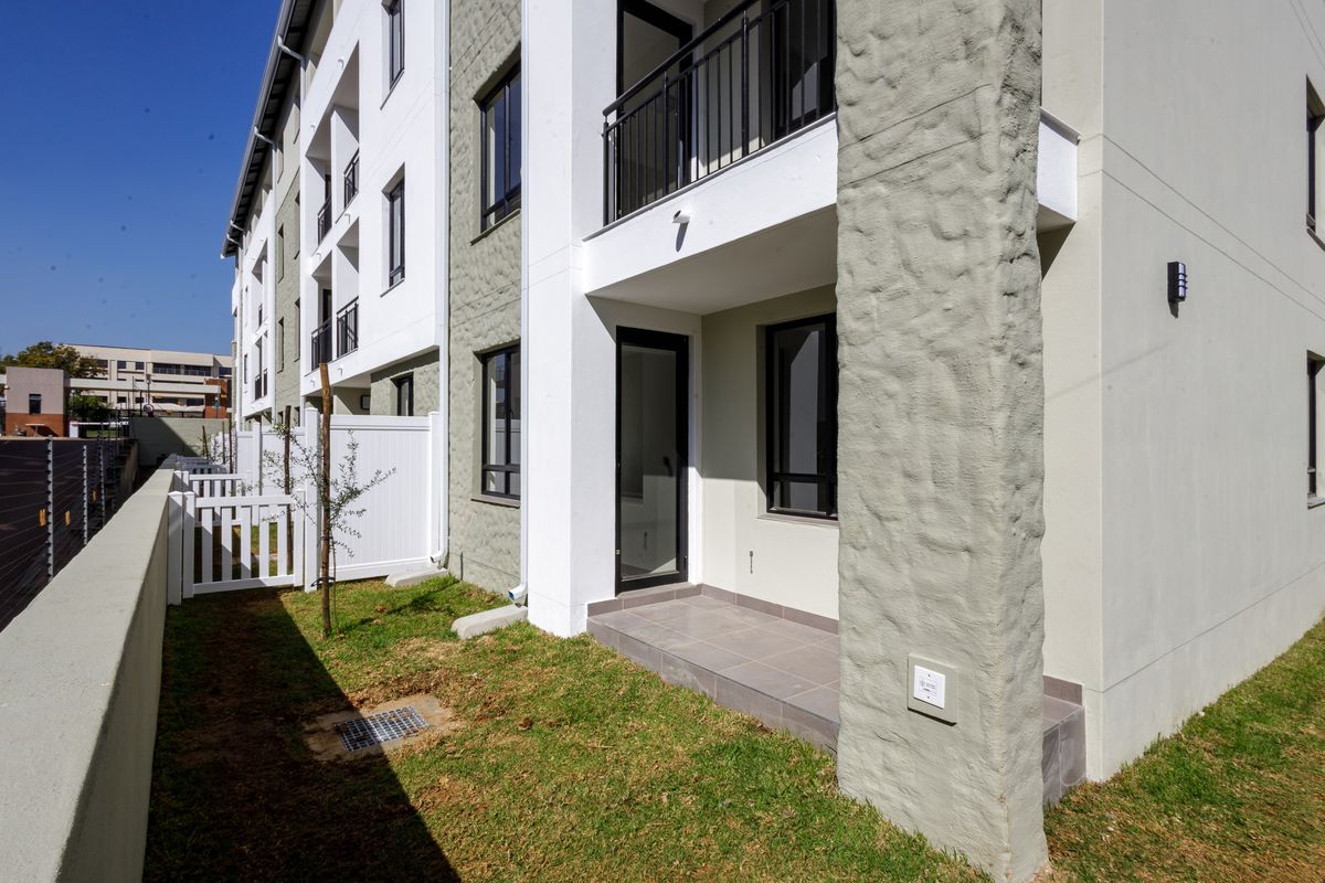 Ground floor apartment exterior featuring a private patio, small garden area, and modern building facade with textured stone accents.