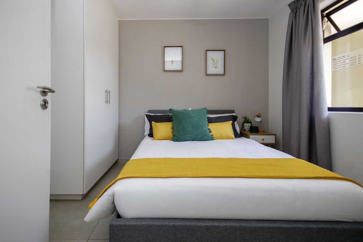 A well-maintained bedroom featuring built-in cupboards, neutral wall finishes, and a window with curtaining.