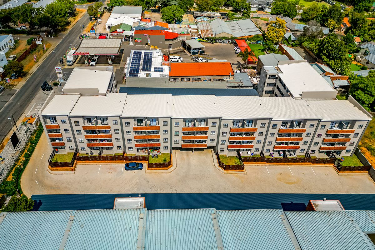 Aerial view of a multi-story apartment complex featuring metal roofing, private balconies, and an adjacent paved parking area.