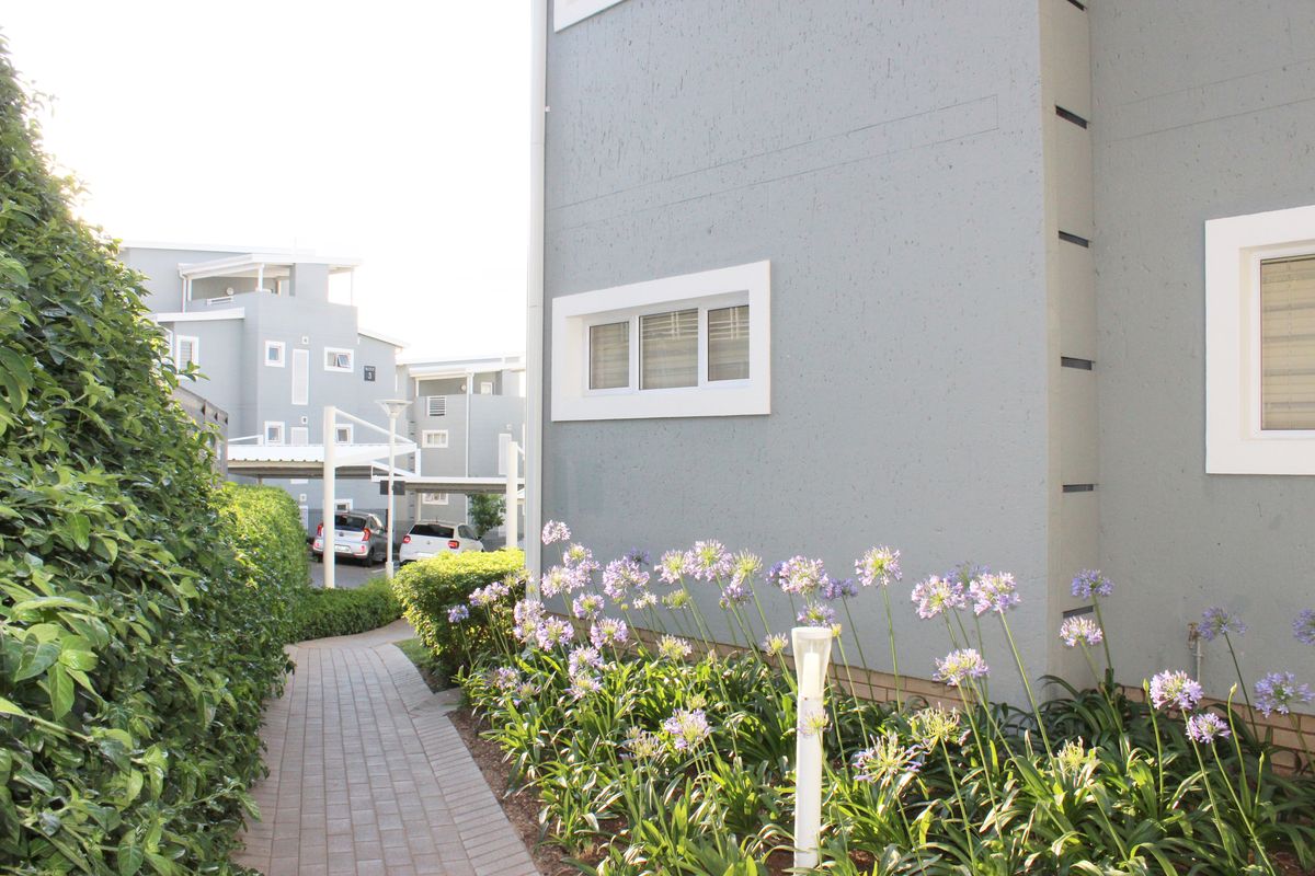 A well-maintained paved walkway leads alongside the apartment building, featuring neat landscaping and exterior lighting.