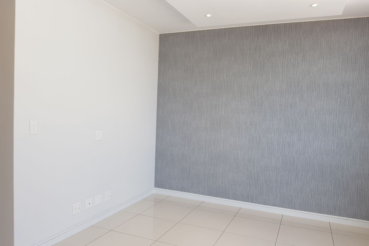 A bright, empty living area featuring modern tiled flooring, recessed downlights, and a stylish grey textured feature wall.