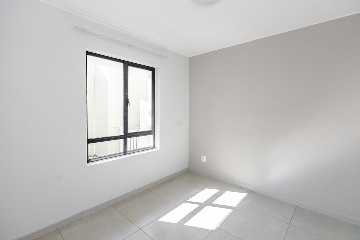 A bright, empty bedroom featuring neutral wall tones, tiled flooring, and a modern black-framed window.