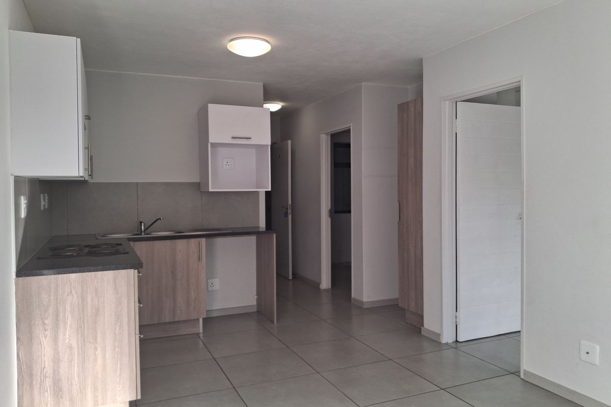 A functional kitchen area featuring light wood-finish cabinetry, dark countertops, a built-in hob, and tiled flooring, leading into a hallway with access to other rooms.