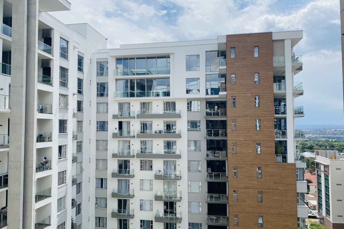 Exterior view of a modern apartment building featuring multiple balconies with glass balustrades and a mix of white and wood-look cladding.