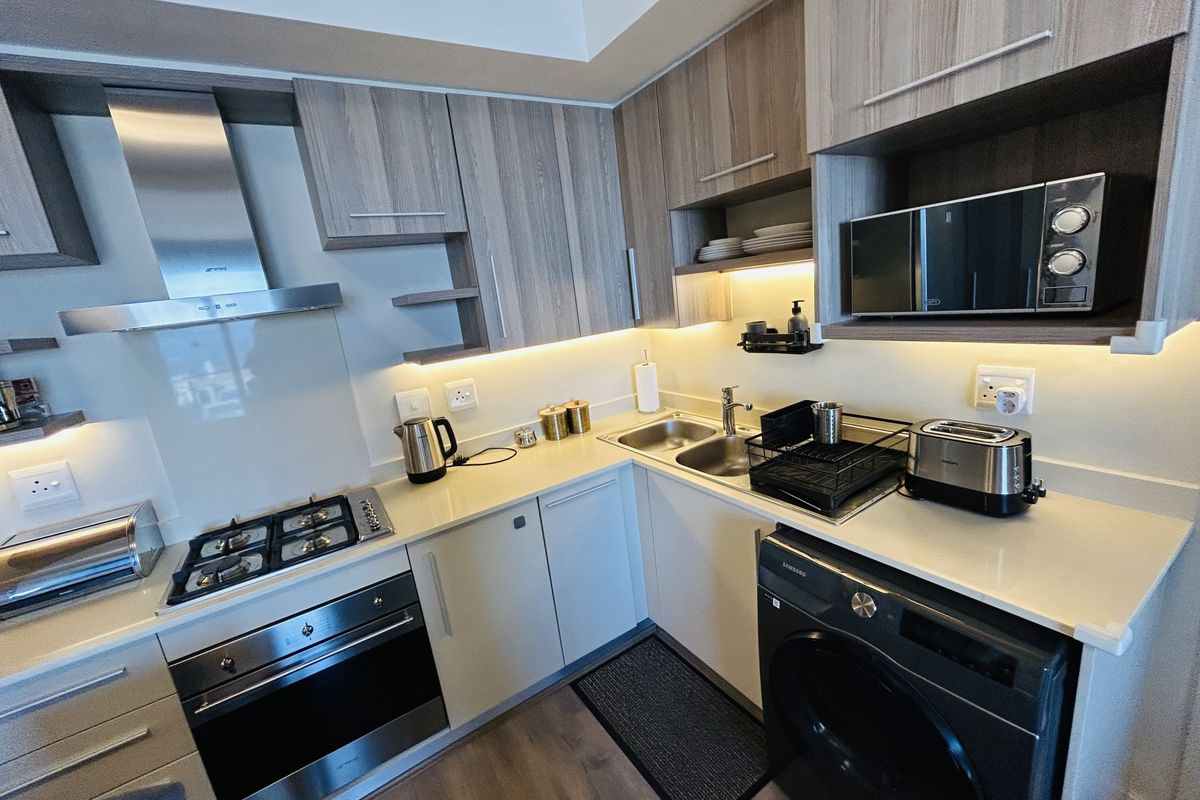 Modern kitchen featuring stone countertops, integrated appliances including a gas hob, oven, extractor fan, and built-in microwave with ample cabinetry and under-cabinet lighting.