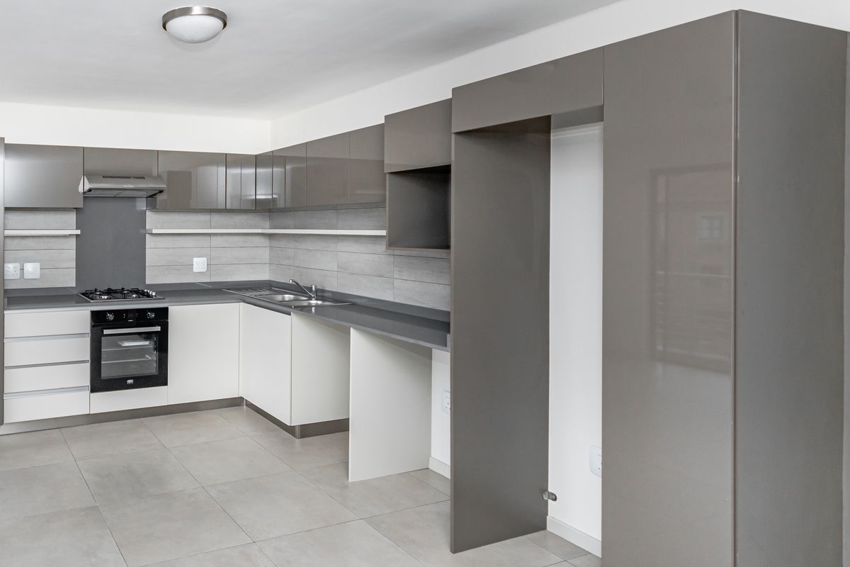 Modern kitchen featuring high-gloss cabinetry, stone countertops, built-in oven, gas hob, extractor fan, and neutral tiled flooring.
