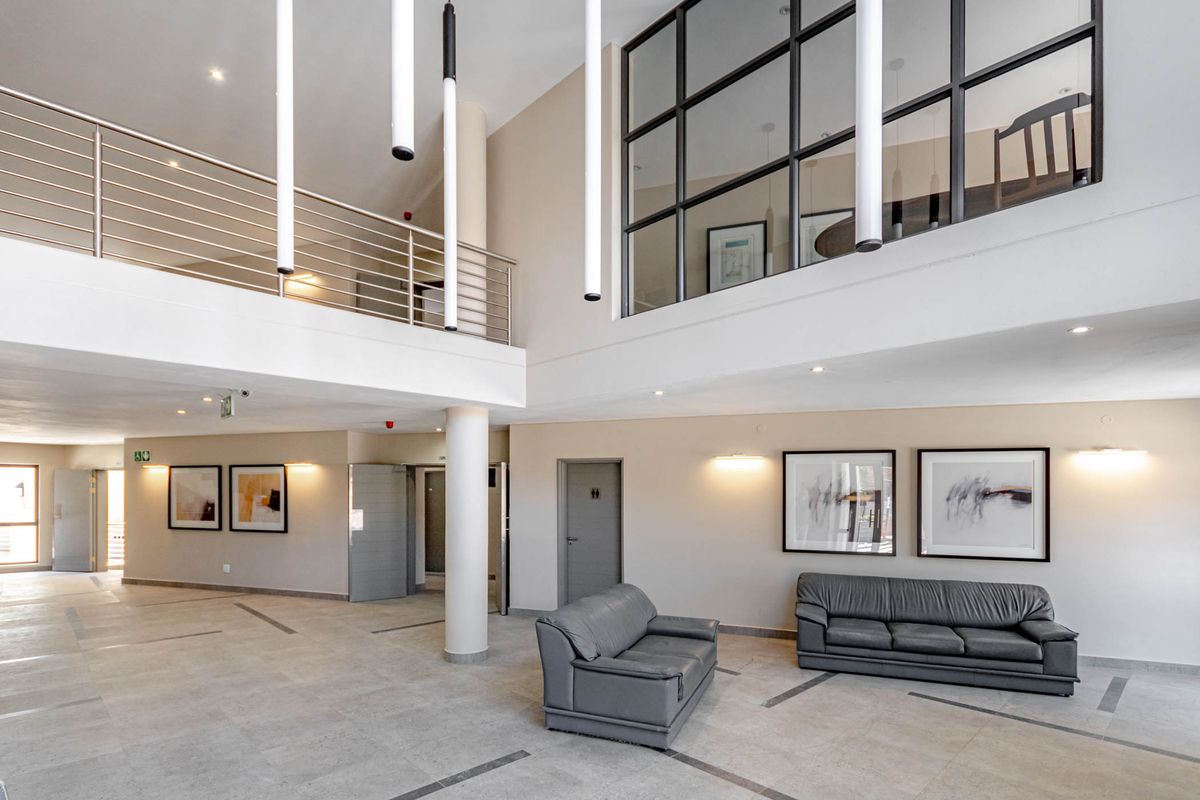 Spacious double-volume living area featuring a mezzanine level, modern pendant lighting, large glass partitions, and high-quality tiled flooring.