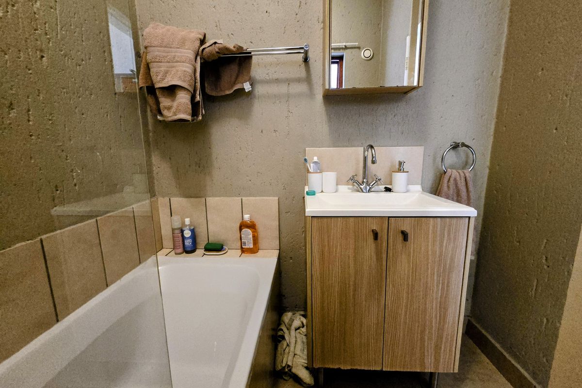 A functional bathroom featuring a bathtub with a glass screen, a vanity cabinet with a basin, and a wall-mounted mirror cabinet.