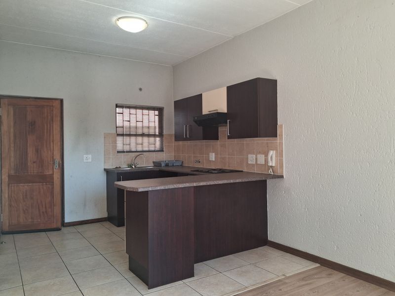 A functional kitchen featuring dark wood cabinetry, laminate countertops, a built-in hob with extractor fan, and tiled flooring.