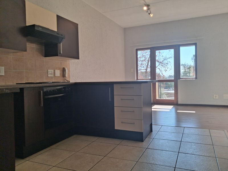 Open-plan kitchen and living area featuring dark cabinetry, built-in oven, tiled and laminate flooring, and access to a balcony through a sliding glass door.