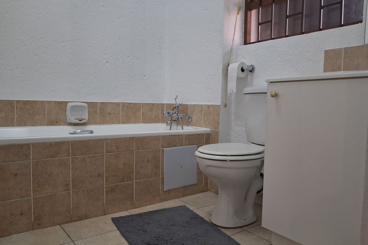 A functional bathroom featuring a tiled bathtub surround, standard toilet, and vanity cabinet with neutral finishes.