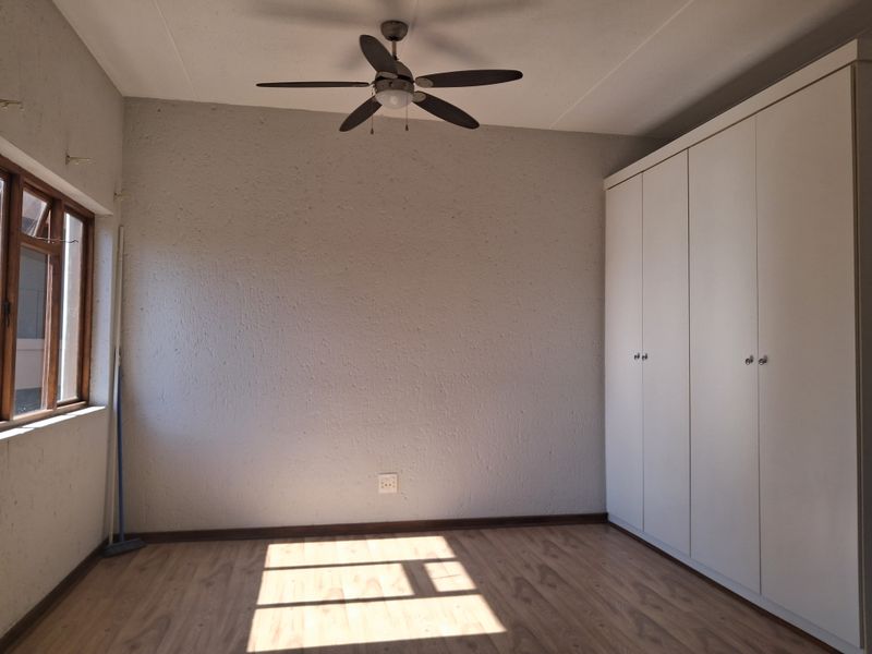A bright, empty bedroom featuring laminate flooring, a ceiling fan, and ample built-in cupboard storage space.