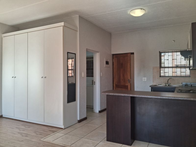 An open-plan living and kitchen area featuring built-in cupboards, a breakfast bar, and a mix of tiled and laminate flooring.