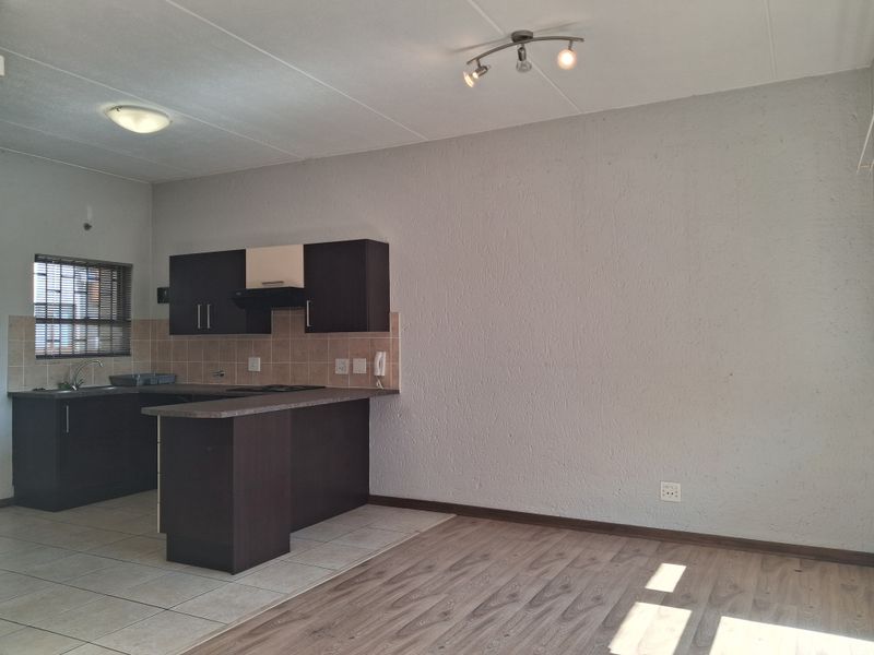 Open-plan living area featuring a compact kitchen with dark cabinetry, tiled backsplash, and a combination of laminate and ceramic tile flooring.