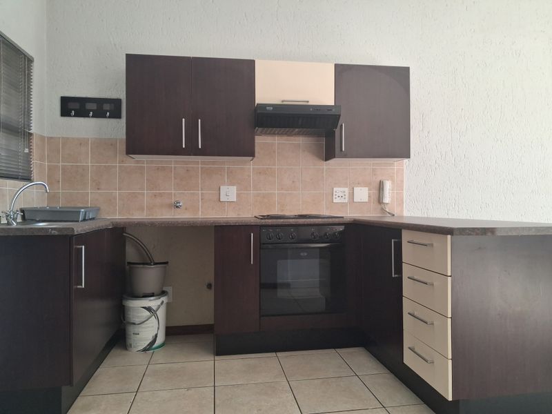 A functional kitchen featuring dark and light cabinetry, built-in oven with hob, extractor fan, tiled backsplash, and ceramic floor tiles.