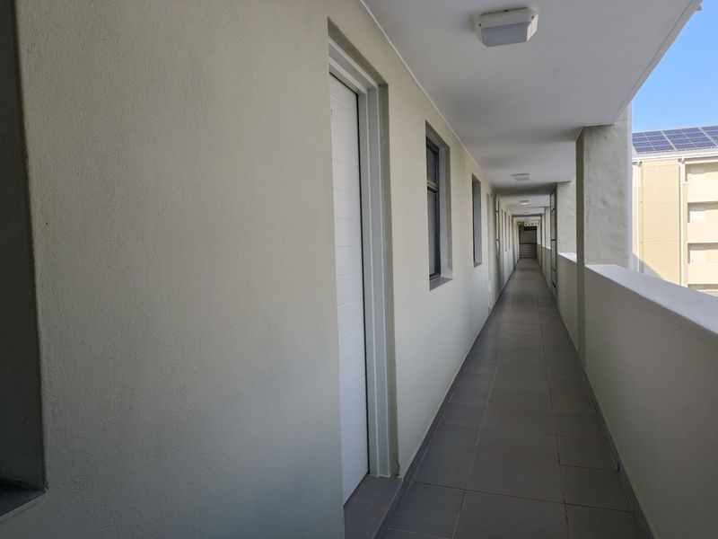 A clean, well-maintained outdoor apartment corridor featuring tiled flooring, neutral wall finishes, and multiple unit access points.