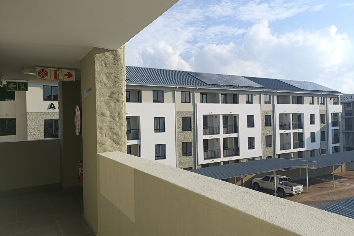 View from a covered walkway overlooking the apartment complex, featuring modern architecture, solar panels, and dedicated covered parking bays.