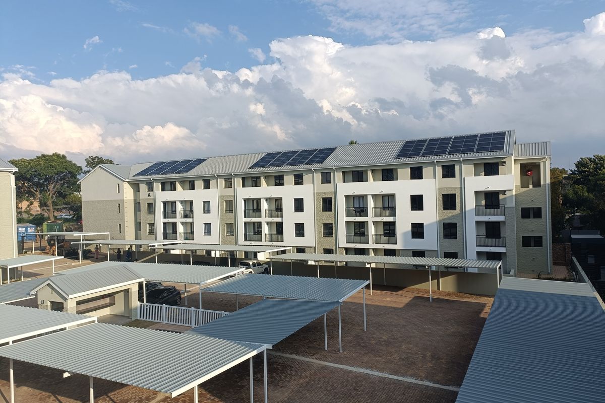 Aerial view of a modern apartment complex featuring covered parking bays, paved grounds, and solar panels installed on the roof.