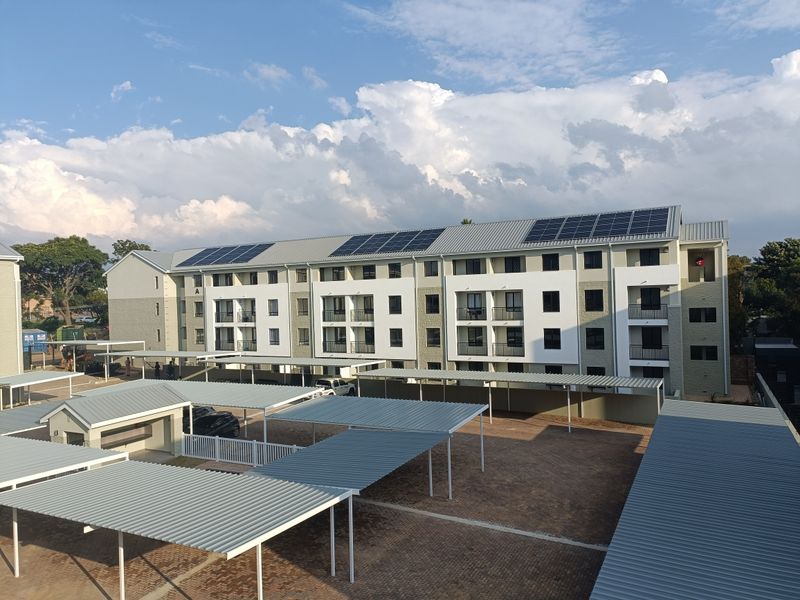 Aerial view of a modern apartment complex featuring covered parking bays, paved grounds, and solar panels installed on the roof.