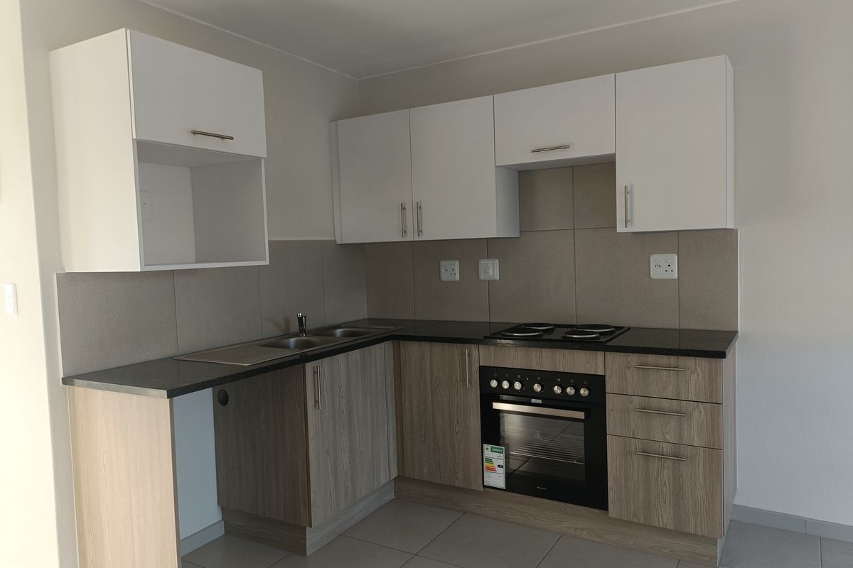Modern kitchen featuring light wood-grain lower cabinets, white upper cabinetry, dark countertops, built-in oven, electric hob, and neutral tiled backsplash.
